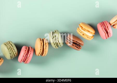 Assorted French macarons in various colors arranged diagonally on a mint green background. Minimal, vibrant, and sweet-themed. Stock Photo