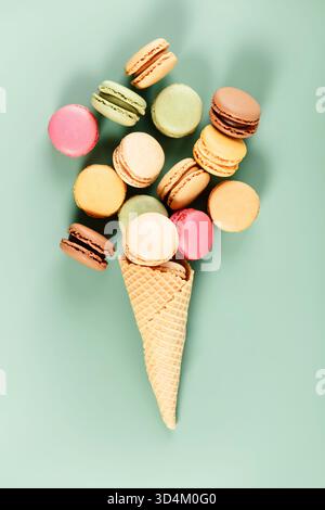 Creative flat lay of assorted macarons arranged in a waffle cone like ice cream, on a soft mint green background. Stock Photo