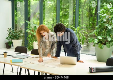 Two colleagues reviewing blueprints on a coworking table Stock Photo