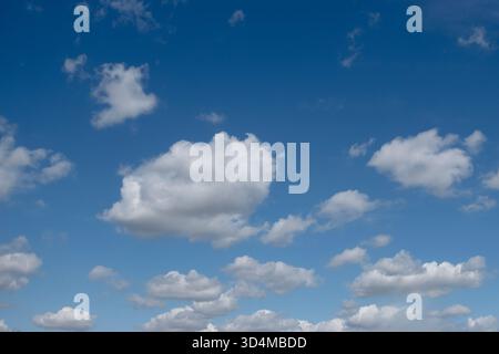 White fluffy clouds scattered across a blue sky on a bright sunny day representing peace and tranquility Stock Photo