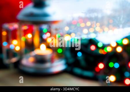 Blurred Christmas background, defocused lantern with a burning candle and shining garland on the windowsill and winter forest outdoor Stock Photo
