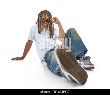 Young man with dreadlocks and sunglasses sitting in casual attire against a white background Stock Photo