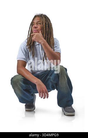 Young man with dreadlocks crouching and appearing thoughtful on a white background Stock Photo