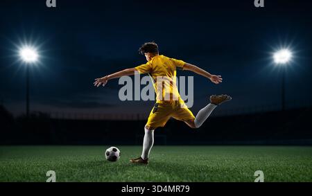 Composite image of soccer player in yellow gear striking the ball with precision under lights Stock Photo