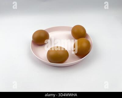 Four brown eggs arranged on a light pink/pale mauve, shallow plate or dish. Stock Photo