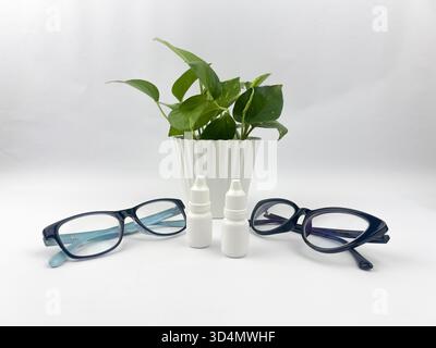 A symmetrical still life composition centered around eyecare and wellness, featuring two pairs of eyeglasses, two small white dropper bottles Stock Photo