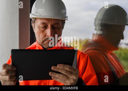 Civil engineer in safety jacket and hardhat using digital tablet at construction site, symbol of technology, control, and modern project management. S Stock Photo