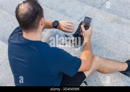Man with disability, wearing a leg prosthesis, sitting on the street steps, looking at a wrist watch. Physical impairment and mobility concept. Stock Photo