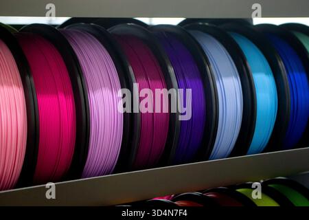 Many spools with multi-colored plastic for 3D printing. Spools with pink, red, burgundy, purple blue plastic wire for 3D printer. Components for 3D printing. Accessories for 3D printer. FDM technology Stock Photo