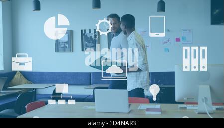 Walking two colleagues exchanging notes near table in office, laptop, green folder, sweater Stock Photo