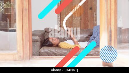 Reclining Chinese woman holding phone overhead at home on brown leather sofa with graphic overlays Stock Photo