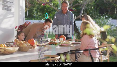 Gathering multigenerational family sharing meal on covered patio, with long white dining table Stock Photo