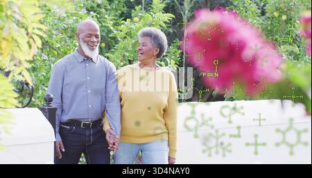 Walking couple holding hands, talking on garden path in blue shirt, mustard sweater with white wall Stock Photo