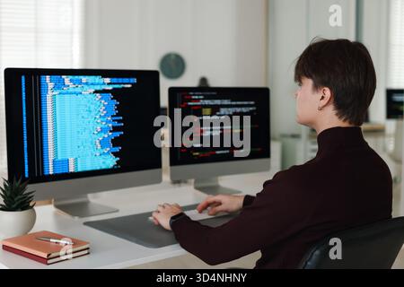 Programmer working on computer with dual monitors at white table in office Stock Photo