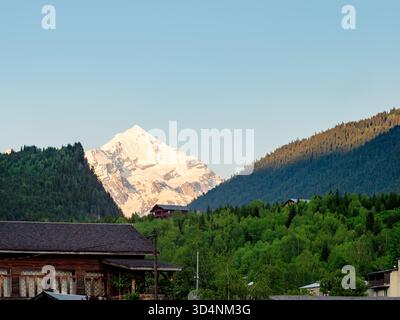 snow-covered mountain peak lit by setting sun over Mestia town in Samegrelo-Zemo Svaneti province of Georgia in summer evening Stock Photo