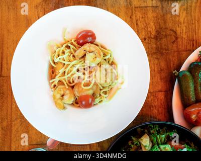 top view of spaghetti pasta with fried king prawns on white plate on wooden table in outdoor fish market cafe in Batumi city, Georgia Stock Photo