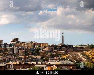 cloudy sky over Cascade monument and houses in Yerevan city, Armenia on sunny summer evening Stock Photo