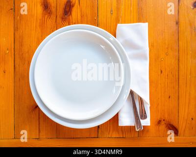 top view of two empty white plates and knife and fork in napkin served on wooden table Stock Photo