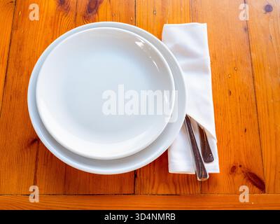 above view of two empty white plates and knife and fork in napkin served on wooden table Stock Photo