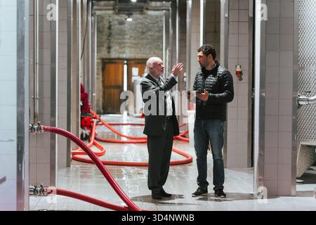 Two men engage in a lively discussion inside a spacious and modern wine cellar during the day. Stock Photo