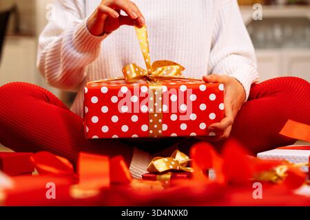 Female unpacking red Christmas gift box wrapped in white polka dot paper. Stock Photo