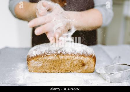 Close-up hands of female chef sprinkles rectangular rye bread with flour for long storage Stock Photo