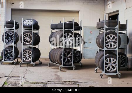 Car tires and alloy wheels stored on metal racks in auto repair workshop, automotive service and maintenance concept Stock Photo