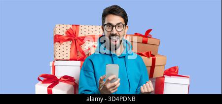 Excited Young Man Holding a Phone Surrounded by Gift Boxes in a Colorful Collage Setting Stock Photo