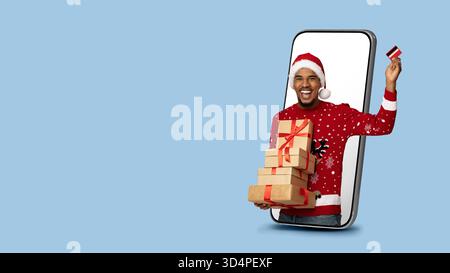 Man in Christmas Sweater Holding Gifts and Card Coming out of Smartphone Screen Stock Photo