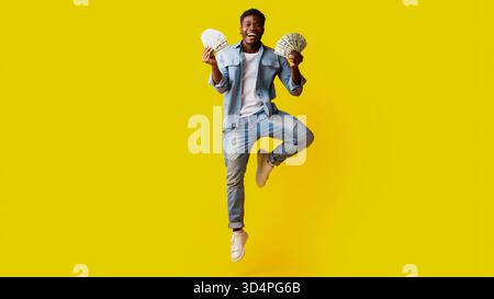 Joyful Young Man Jumping With Money in Hands Against a Bright Yellow Background Stock Photo