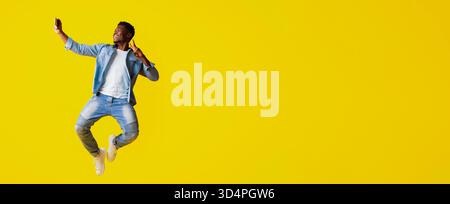 Man Jumping Joyfully While Taking a Selfie on a Bright Yellow Background Stock Photo