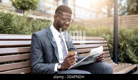 Young Man in a Suit Enjoys Coffee and Reads Newspaper in Park During Daytime Stock Photo