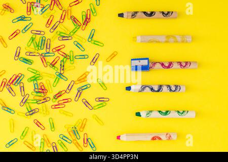 Colorful layout made with paper clips and wax crayons on light yellow background. Minimal school concept. Flat lay style. Top view. Stock Photo