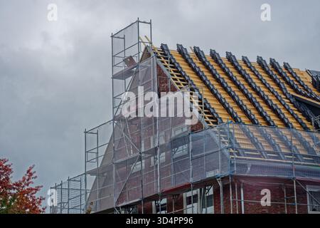 A two story house is wrapped in silver scaffolding from ground to roof, fresh boards and metal frames surround every wall which suggests repair work a Stock Photo