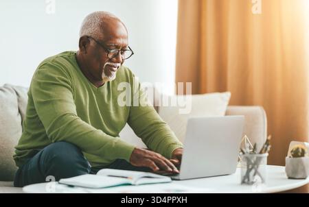 Elderly Man Working on Laptop While Sitting on Couch at Home During Afternoon Stock Photo