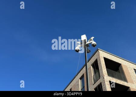 Surveillance cameras are mounted on a tall pole next to a contemporary building under a clear blue sky. The cameras are positioned to monitor the surr Stock Photo