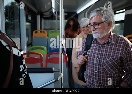 Senior man commuting on bus, standing with backpack Stock Photo