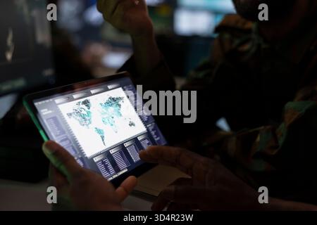 Military officer using tablet device to deploy electronic warfare tools to disrupt enemy communication systems. Soldier operating on high tech infrastructure weapons, close up Stock Photo