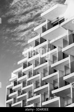 Black and white view of modern stepped apartment building with repeating geometric balconies under a cloudy sky Stock Photo