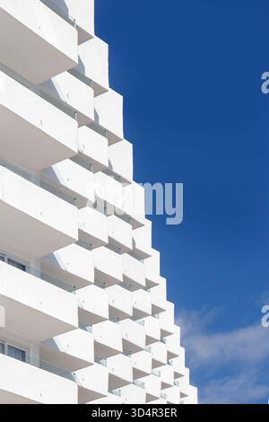Modern white apartment building with geometric balconies under a vibrant clear sky viewed from a low angle Stock Photo