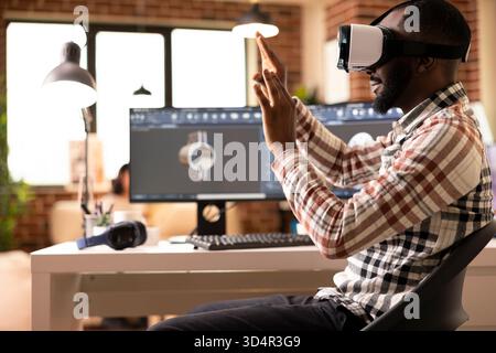 African american freelance developer immersed in VR, prototyping 3D clamp model. Black male engineer using computer aided design tools and virtual reality headset to craft precision product design. Stock Photo