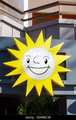 Bright yellow smiling sun cartoon sign with a cartoon face mounted on a building exterior under natural light Stock Photo