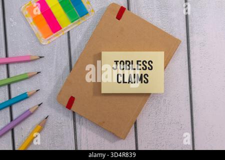 Jobless claims text on white paper from a notepad on a wooden background. wooden blocks magnifier Stock Photo