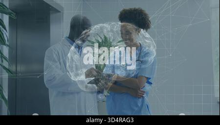 Reviewing doctor using tablet in hall nurse wearing blue scrubs lab coat stethoscope brain hologram Stock Photo