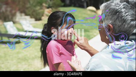 Applying senior man gently touching child nose at backyard, with pink rash guard, white cream Stock Photo