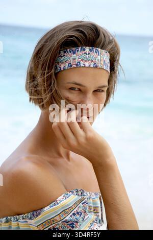 Headshot of beautiful young woman in shoulder free summer blouse and hair band, while looking at camera and soft touching her face. Portrait Stock Photo