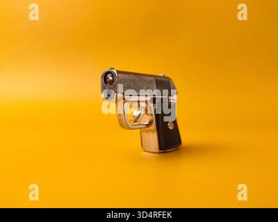 A small handgun is on a yellow background. Stock Photo