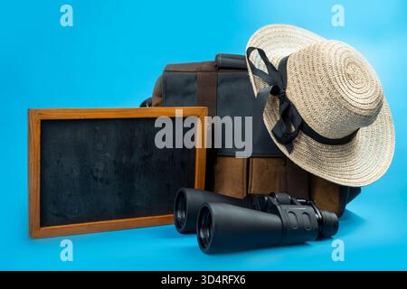 Chalkboard and Canvas bag with binoculars and a straw hat with a black ribbon on a blue background. Mockup or Copy space. Concept of travel, summer, o Stock Photo
