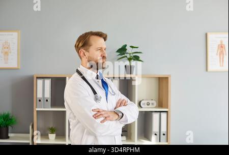 Doctor standing in medical office wearing white lab coat and stethoscope, posing, looking Stock Photo