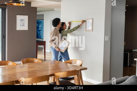Hanging Diverse couple positioning framed picture on modern dining room wall, using yellow tape Stock Photo